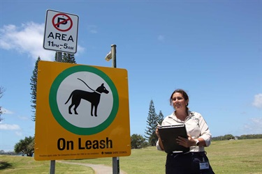 Council ranger in park next to dogs on leash sign